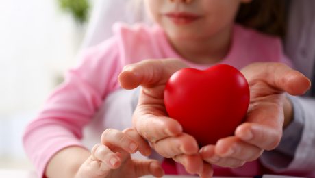 Les mains d’un médecin pédiatre et d’une enfant tenant un cœur rouge.