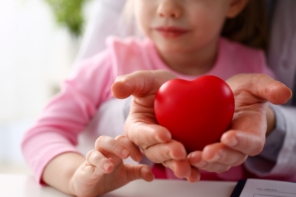 Les mains d’un médecin pédiatre et d’une enfant tenant un cœur rouge.
