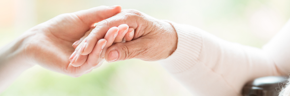 Gros plan sur un geste tendre entre deux générations. Jeune femme tenant la main d'une femme âgée. 